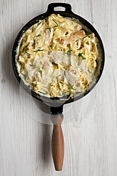 Homemade Chicken Fettuccine Alfredo in a cast-iron pan on a white wooden background, overhead view. Flat lay, top view, from above