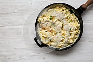 Homemade Chicken Fettuccine Alfredo in a cast-iron pan on a white wooden background, overhead view. Flat lay, top view, from above