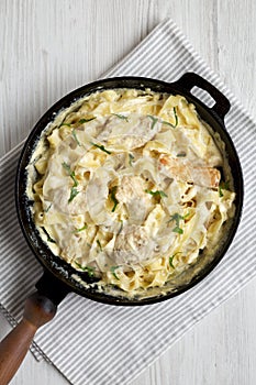 Homemade Chicken Fettuccine Alfredo in a cast-iron pan on a white wooden background, top view. Flat lay, overhead, from above.