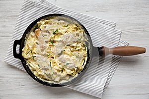 Homemade Chicken Fettuccine Alfredo in a cast-iron pan on a white wooden surface, overhead view. Flat lay, top view, from above