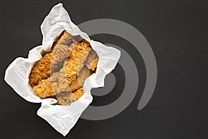 Homemade chicken fingers in paper box on a black background, top view. Flat lay, overhead, from above. Copy space