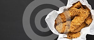 Homemade chicken fingers in paper box on a black background, top view. Flat lay, overhead, from above. Space for text