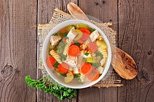 Homemade chicken noodle soup with vegetables, top view on a wood background