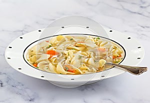 Homemade chicken noodle soup in white bowl with spoon on marble background