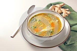 Homemade chicken soup with vegetables, ginger and parsley in a bowl, green napkin and spoon on a gay white table, copy space,