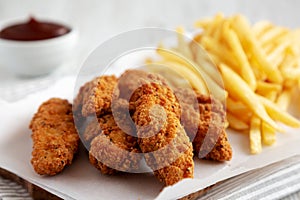 Homemade Chicken Tenders with French Fries and BBQ Sauce on a rustic wooden board, side view. Close-up