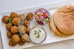Homemade chickpea Falafel balls in a white plate with salad and tahini sauce pitta bread against white background