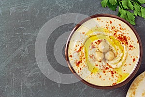 Homemade chickpea hummus bowl decorated with boiled chickpeas, herbs, olive oil and pita bread over gray background