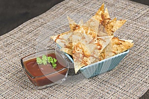 Homemade chips made from pita bread with cheese, herbs, spices and olive oil in turquoise square bowl and red dip sauce