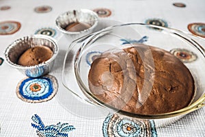 Homemade chocolate cake and cupcakes on the table. round baked chocolate cake in glass baking bowl. Brown muffins in foiled baking