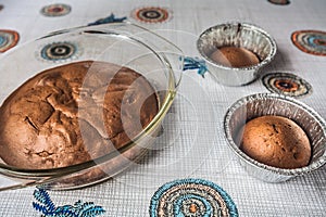 Homemade chocolate cake and cupcakes on the table. round baked chocolate cake in glass baking bowl. Brown muffins in foiled baking