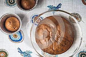 Homemade chocolate cake and cupcakes on the table. round baked chocolate cake in glass baking bowl. Brown muffins in foiled baking