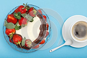 Homemade chocolate cake decorated with fresh strawberries on glass plate and cup of coffee with saucer