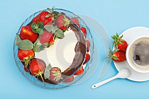 Homemade chocolate cake decorated with fresh strawberries on glass plate and cup of coffee with saucer