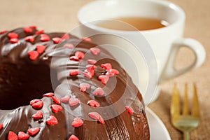 Homemade chocolate cake decorated with small caramel hearts and cup of tea
