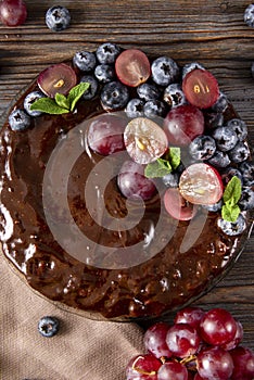 Homemade chocolate cake with fresh berries  grapes and blueberries, mint on a beige towel on a wooden brown background, berry pie