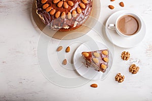 Homemade chocolate cake with milk cream, caramel and almonds on white wooden background. cup of coffee