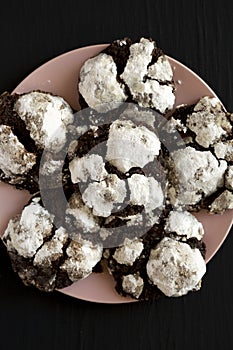 Homemade Chocolate Crinkle Cookies on a pink plate on a black surface, top view. Overhead, from above, flat lay