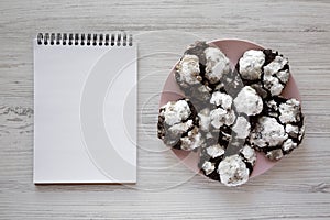 Homemade Chocolate Crinkle Cookies on a pink plate, blank notepad, top view. Flat lay, overhead, from above. Copy space