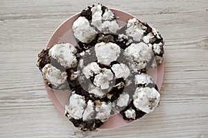 Homemade Chocolate Crinkle Cookies on a pink plate on a white wooden surface, top view. Flat lay, overhead, from above