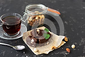 Homemade chocolate fudge garnished with mint leaves and served with tea on a black background. Nuts in the background