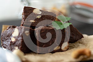 Homemade chocolate fudge garnished with mint leaves and served with tea on a black background. Nuts in the background blurred