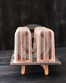 Homemade chocolate ice cream lolly in a plastic mold, on a black wooden background with copy space