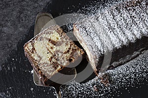 Homemade chocolate marble cake on a slate cutting board covered with icing sugar.