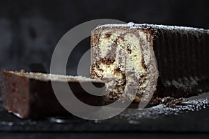 Homemade chocolate marble cake on a slate cutting board covered with icing sugar.