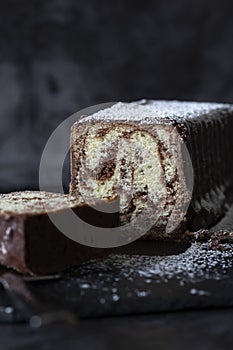 Homemade chocolate marble cake on a slate cutting board covered with icing sugar.