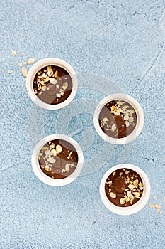 Homemade chocolate pudding in four white ceramic ramekins, decorated with roasted almond slivers, on light blue concrete