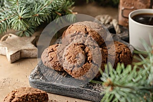 Homemade christmas chocolate cookies on wooden board and coffee on brown festive background with fir tree branches