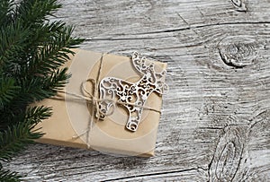 Homemade Christmas gift in kraft paper, wooden Christmas deer ornament, Christmas tree branches on rustic light wooden surface. Fr