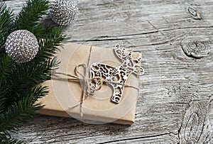 Homemade Christmas gift in kraft paper, wooden Christmas deer ornament, Christmas tree branches on rustic light wooden surface. Fr