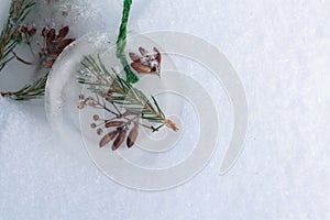 Homemade Christmas tree decorations made of ice and spruce twigs lie on white snow