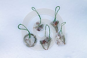 Homemade Christmas tree decorations made of ice and spruce twigs lie on white snow