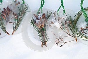 Homemade Christmas tree decorations made of ice and spruce twigs lie on white snow