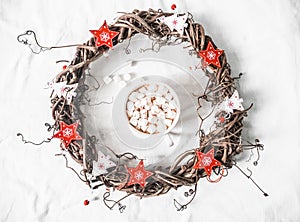 Homemade Christmas vine wreath with red wooden stars and hot chocolate with marshmallows on white background, top view. Copy space