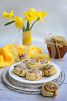 Homemade cinnamon pastries on a white plate, yellow daffodils and a napkin on a light wooden background. Rustic still life