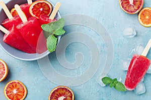 Homemade citrus ice cream or popsicles decorated green mint leaves and orange slices on blue table top view. Frozen fruit juice.