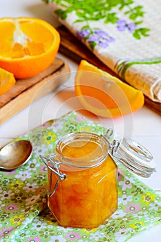 Homemade citrus jam. Sweet orange jam in a glass jar, textile napkin, fresh orange slices on a table. Healthy citrus dessert