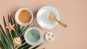 Homemade clay mask recipe concept. Top view cosmetic facial masks in bowls and tropical leaf on peach background. Face skin care,