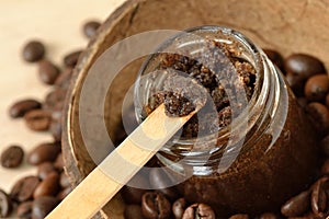 Homemade coffee scrub in a glass jar over coconut shell and coffee beans