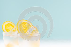 Homemade cold drink with orange liquor, ice cubes in misted shot glass on soft light pastel blue background,  closeup, top, edge.