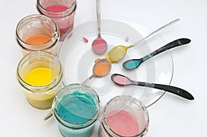 Homemade colorful paints for a baby. Glass jars with dough and food colorants and spoons on a white background. photo