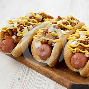 Homemade Coney Island chili dog on a rustic wooden board on a white wooden background, side view. Close-up