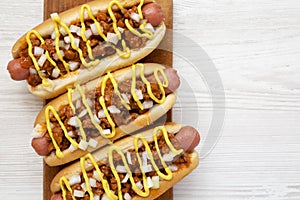 Homemade coney island hot dogs on a rustic wooden board on a white wooden surface, top view. Flat lay, from above, overhead. Copy