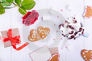 Homemade cookies in shape of heart with Love you lettering on the white wooden table with greeting card, flower, gift box and cup