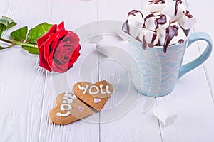 Homemade cookies in shape of heart with Love you lettering on the white wooden table with rose flower and cup of cacao with marshm