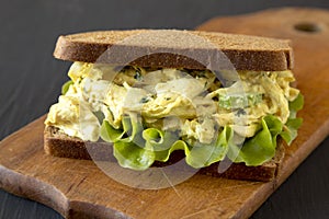 Homemade Coronation Chicken Sandwich on a rustic wooden board on a black surface, low angle view. Close-up